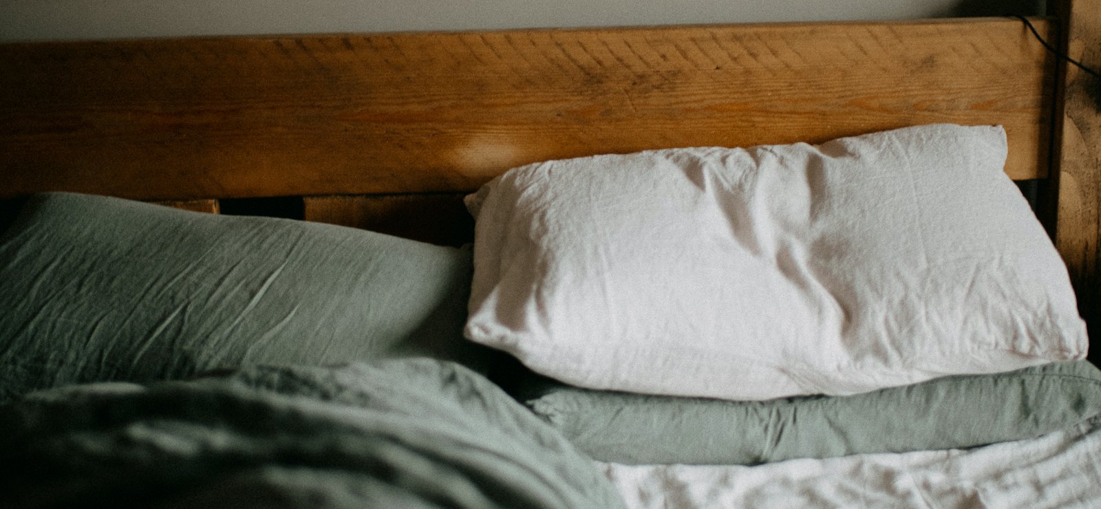 Unmade bed with linen pillows against a wooden headboard